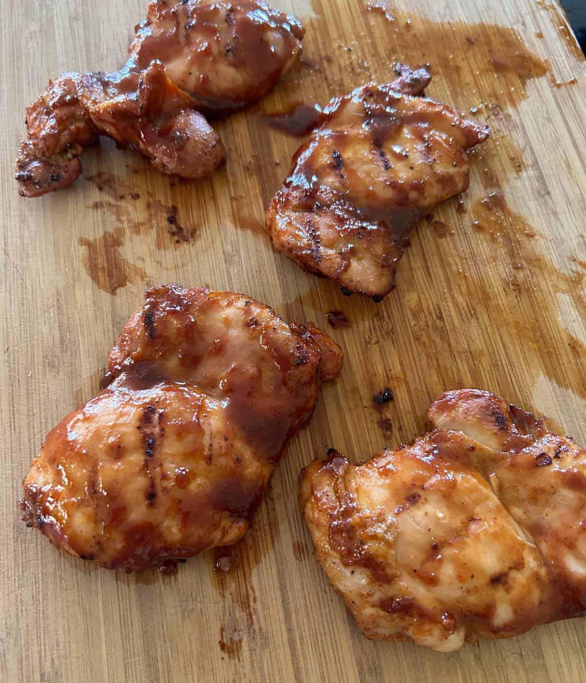 Chicken thighs with bbq sauce on cutting board.
