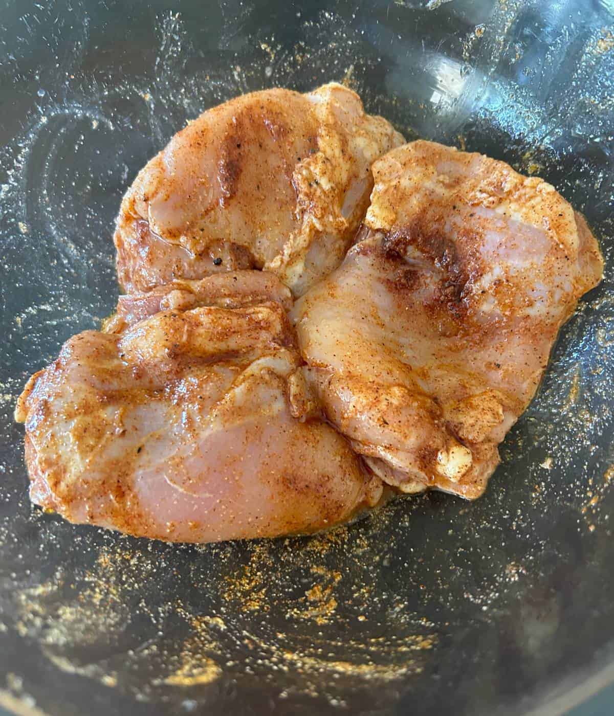 Chicken thighs in marinade in bowl.