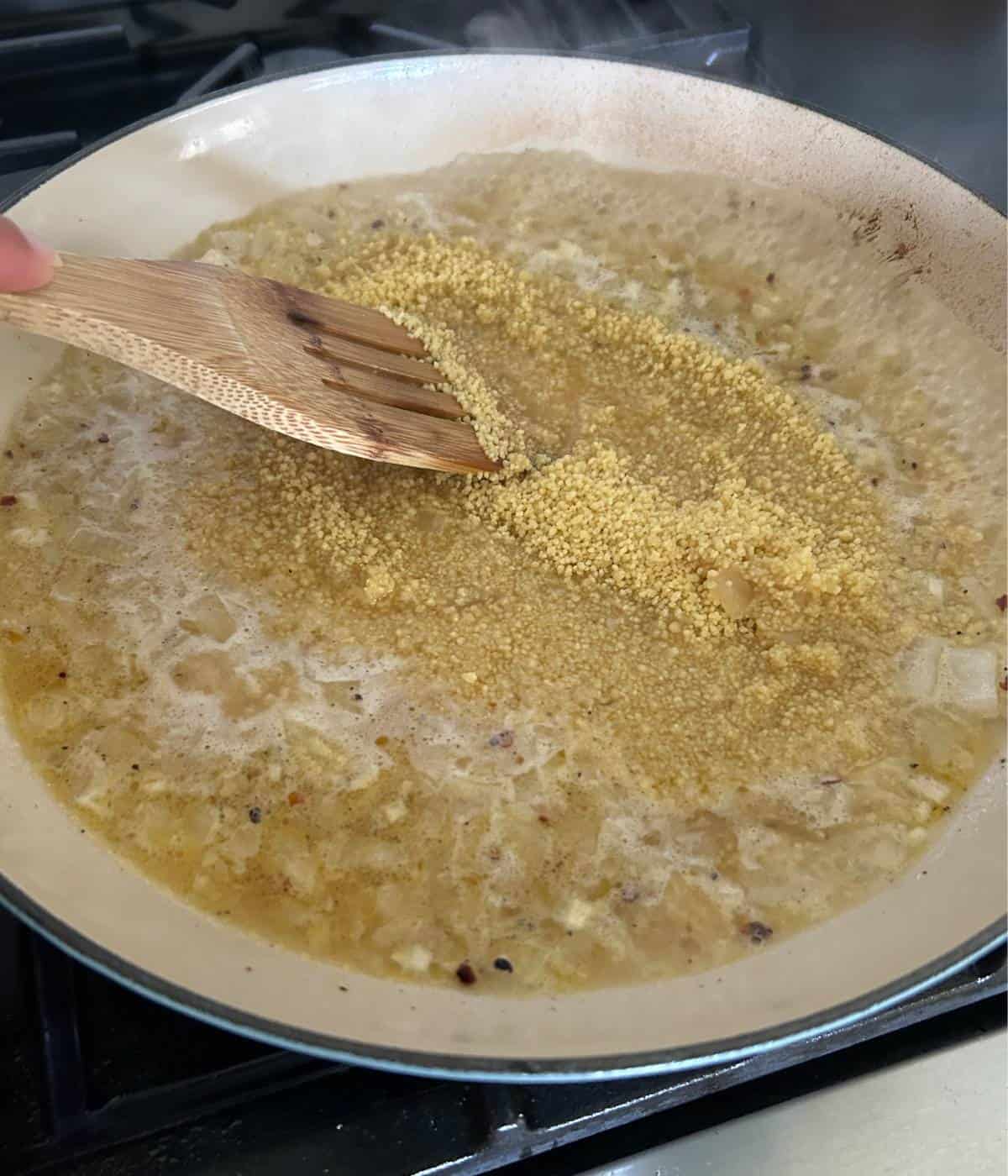Couscous in pan with chicken stock.