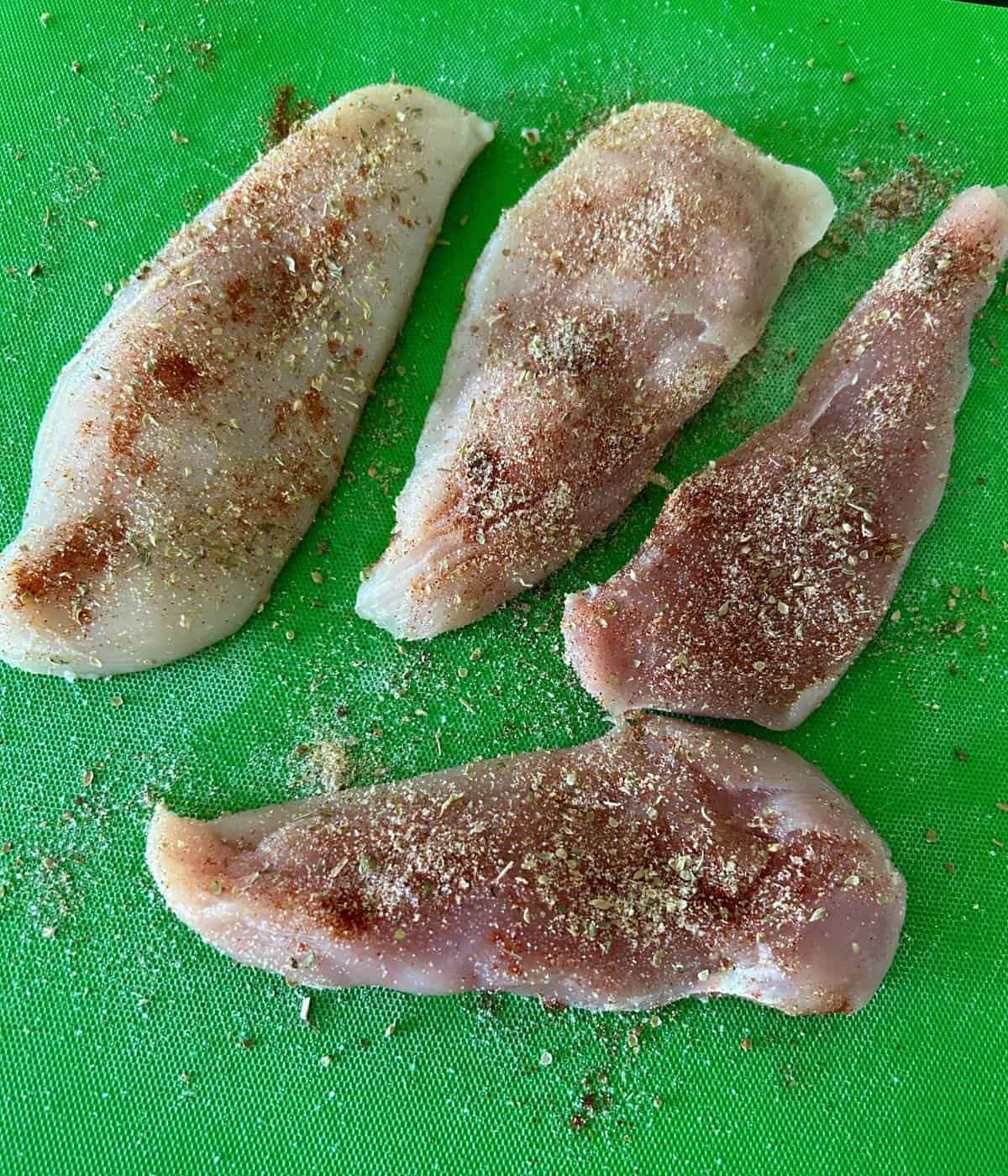Chicken breast with spices on cutting board.
