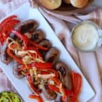 Bratwurst on platter with peppers and onions.
