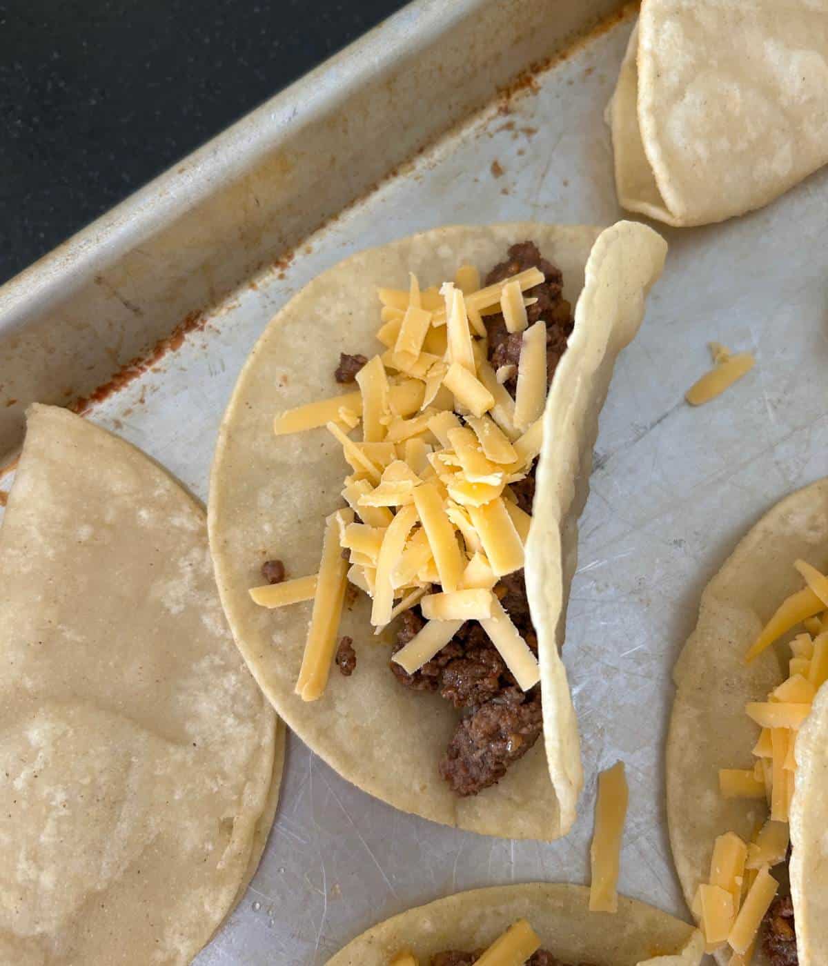 Assembling the ground beef and cheese in tacos.