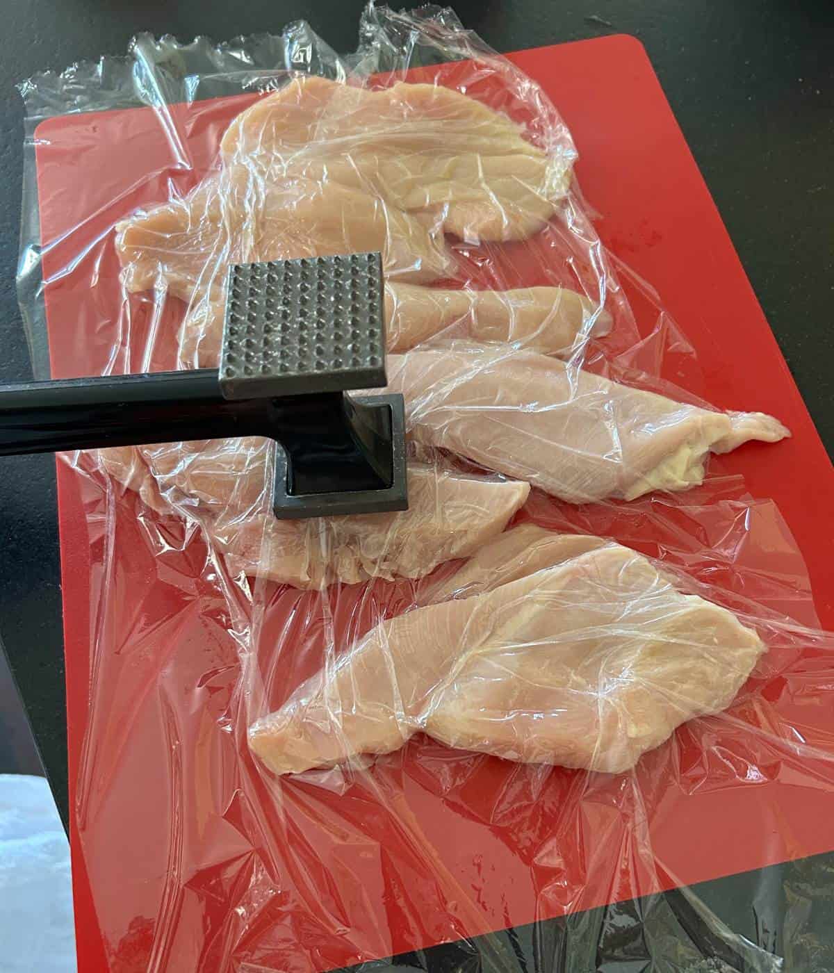 Pounding chicken cutlets on cutting board.