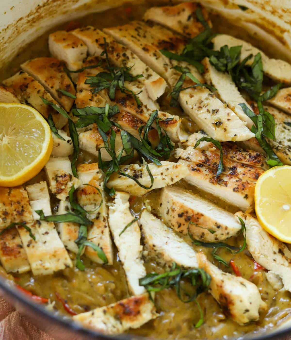 Creamy chicken pesto orzo in pot with lemons.