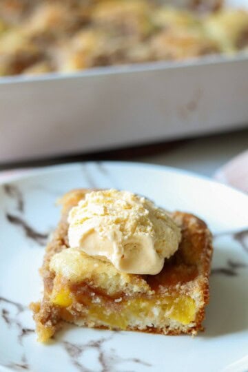 Slice of peach cake on plate with ice cream on top.