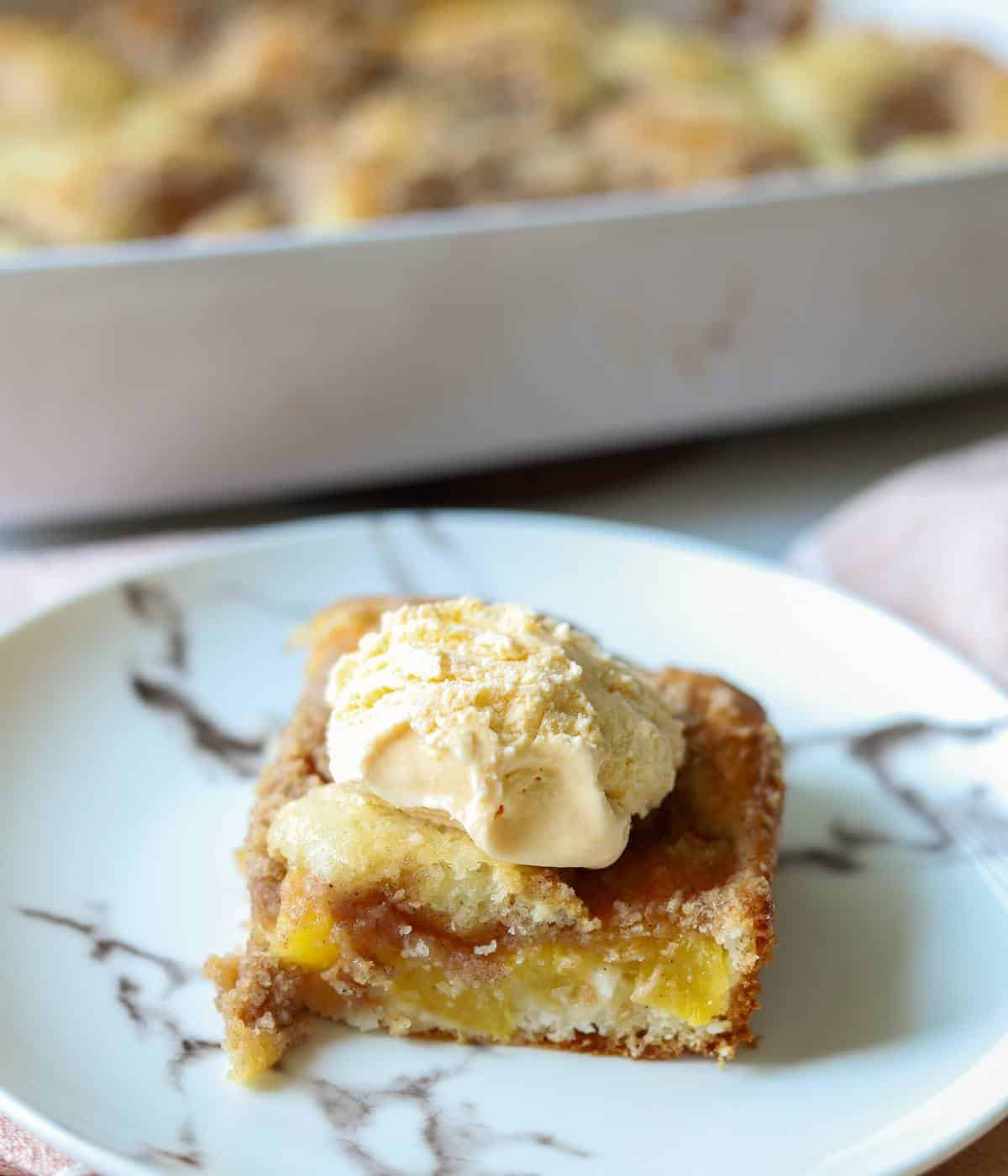 Slice of peach cake on plate with ice cream on top.