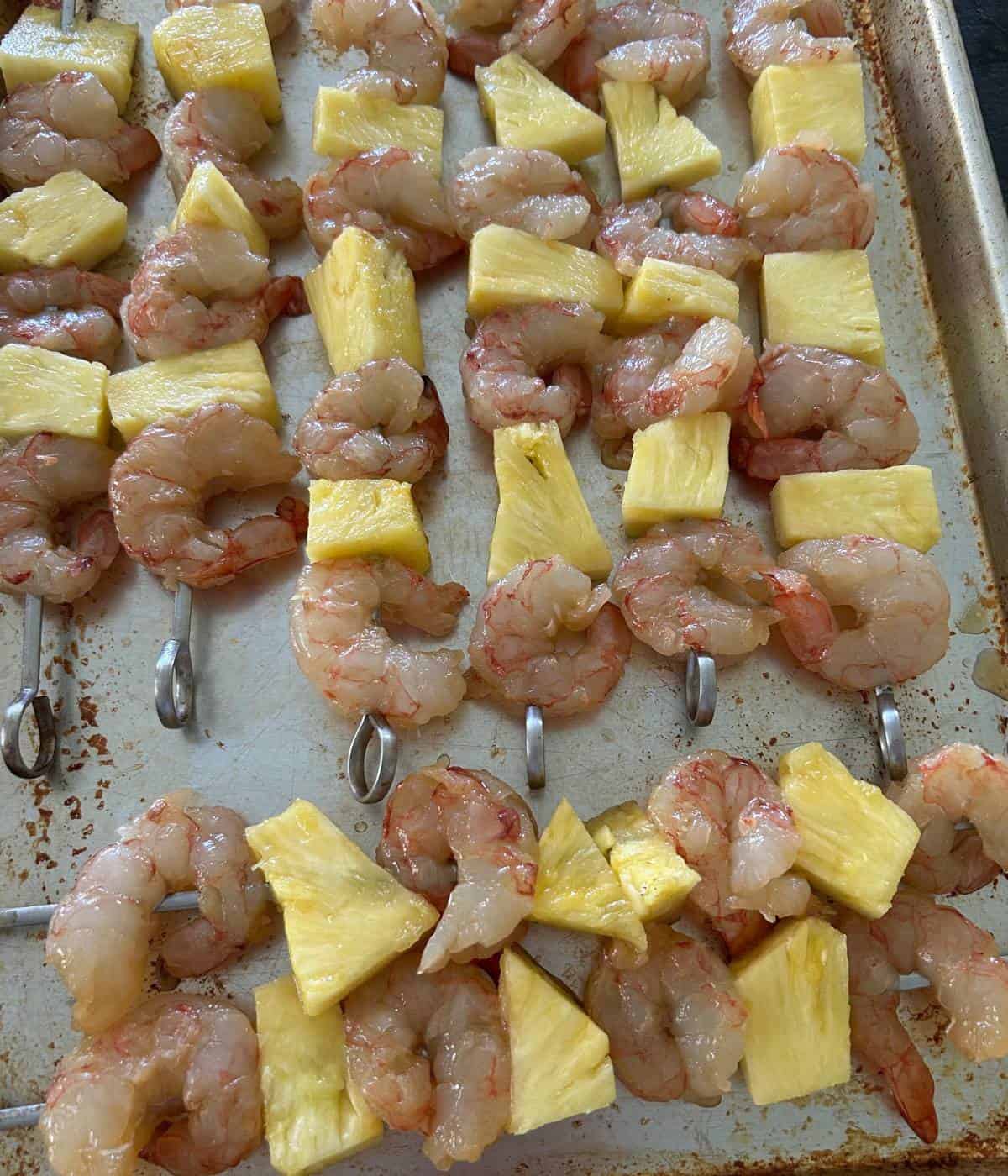 Shrimp and pineapple kabobs on cookie sheet.