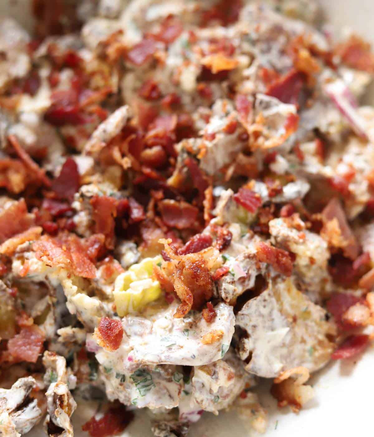 Smashed potato salad in bowl topped with bacon. 