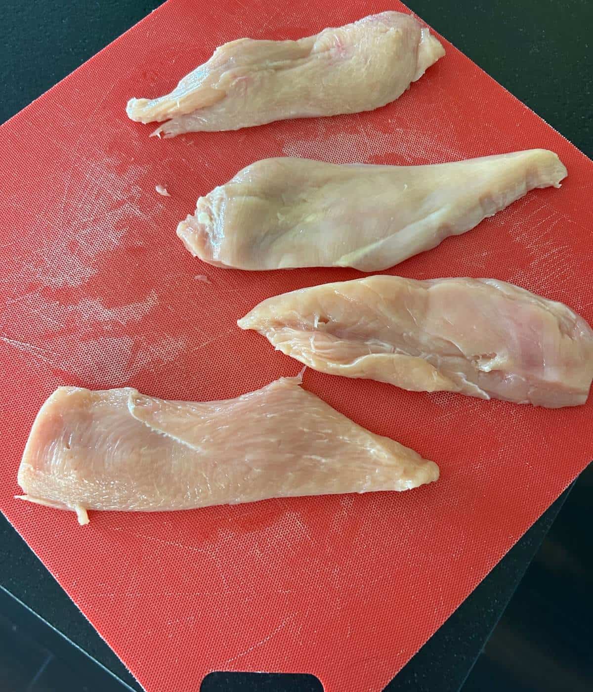 Chicken cutlets on cutting board.
