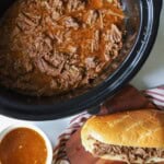Slow Cooker beef in crockpot with sandwiches on the side.