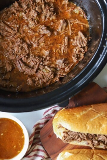 Slow Cooker beef in crockpot with sandwiches on the side.