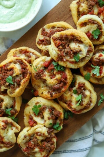Taco crescent pinwheels on platter with avocado crema on side.