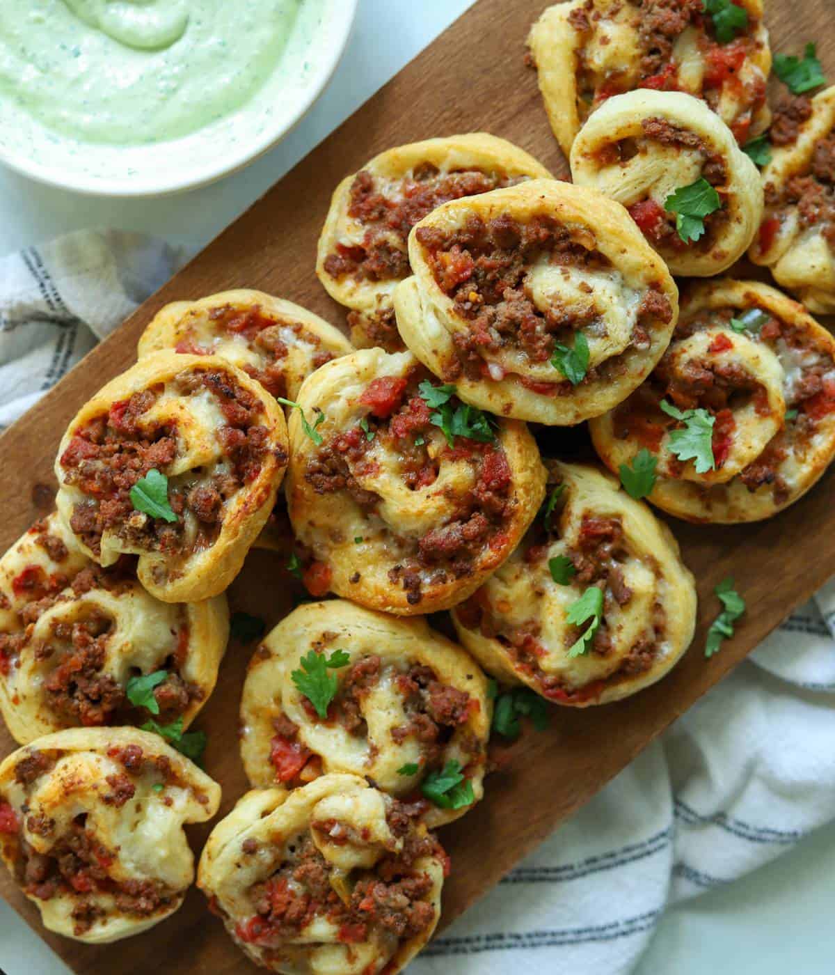 Taco crescent pinwheels on platter with avocado crema on side.