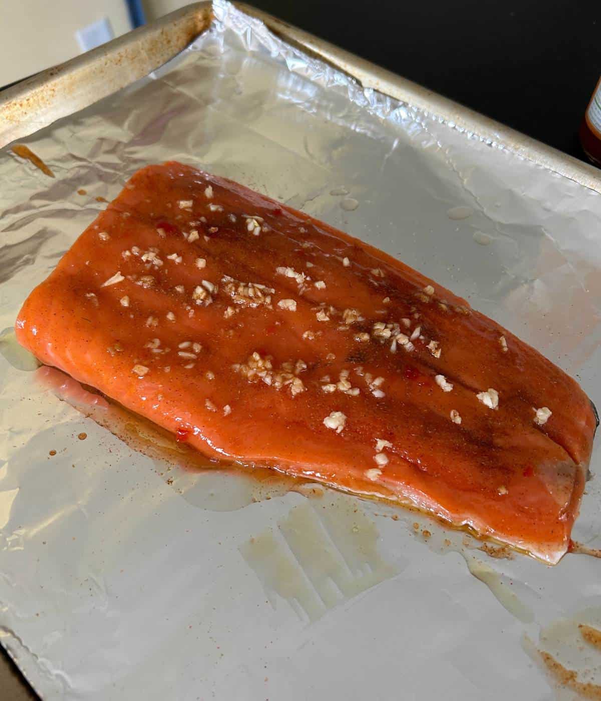 Salmon with chili sauce, garlic and spices on cookie sheet.