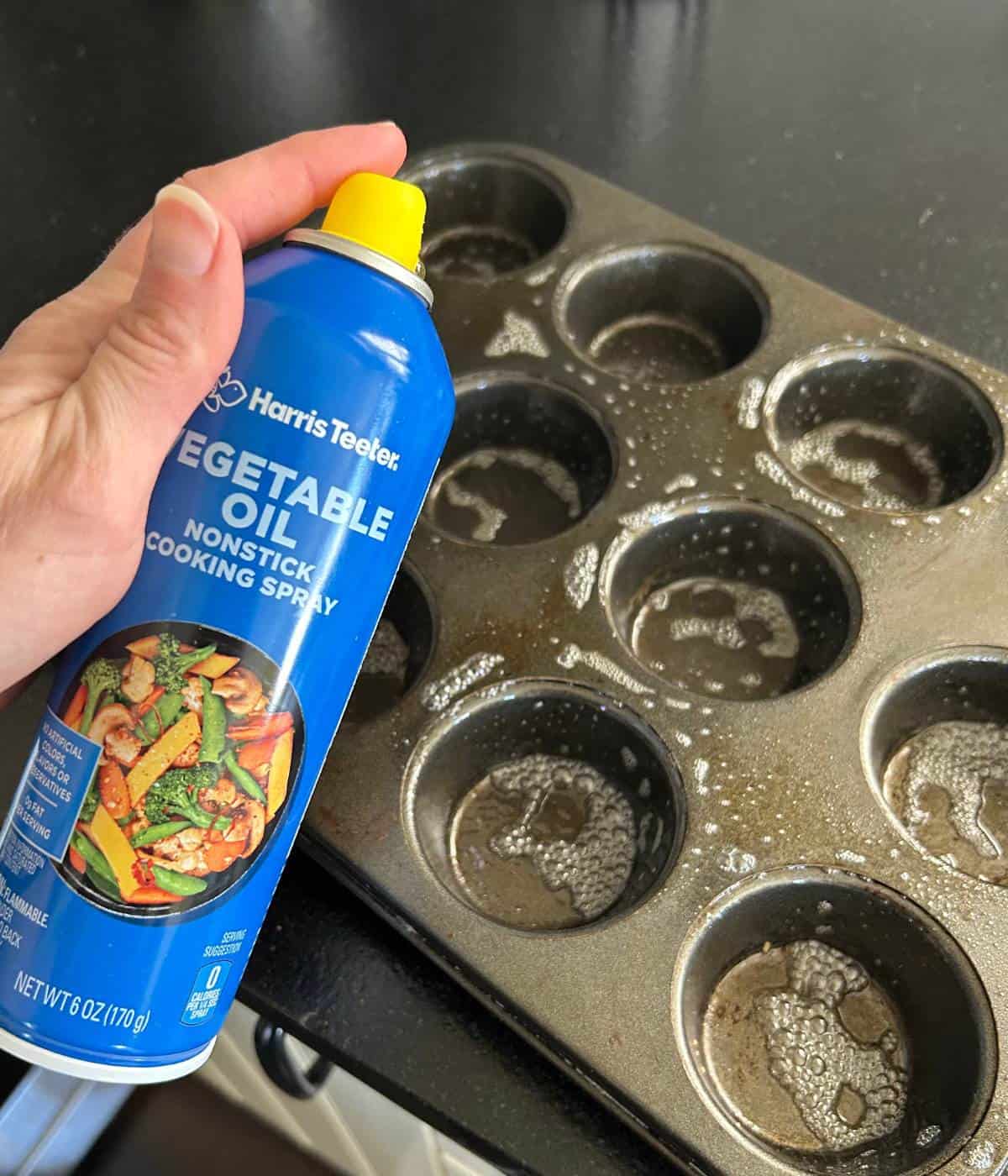 Spraying muffin tin with vegetable oil spray.