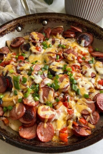 Kielbasa and pierogies topped with cheese in skillet.