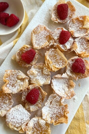 Lemon curd tarts on platter with raspberries.