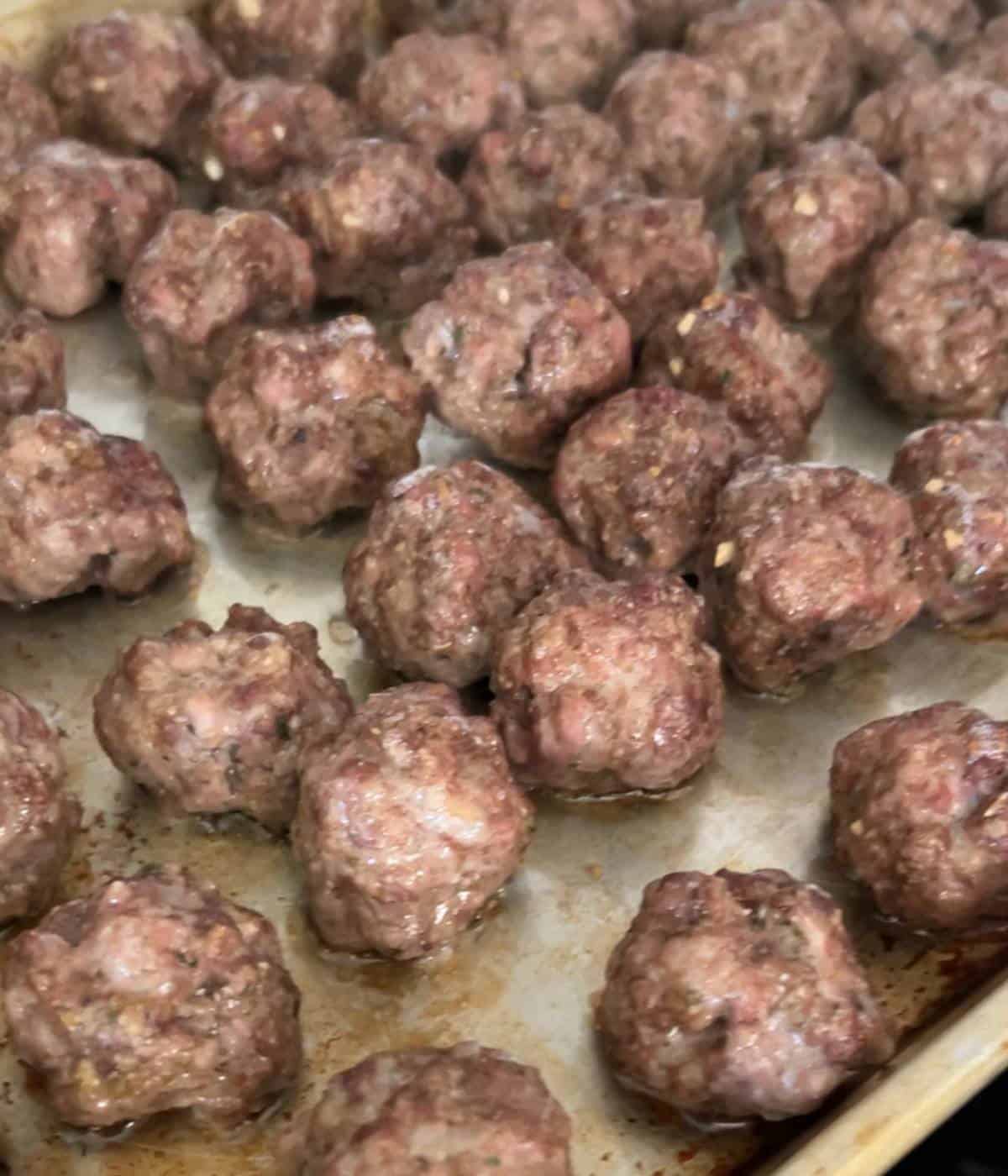 Baked meatballs on cookie sheet.
