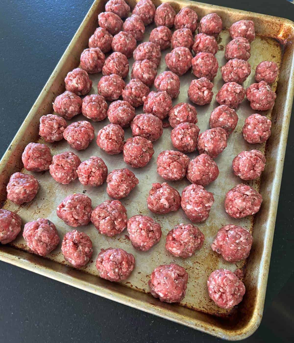 Large batch of meatballs on cookie sheet.