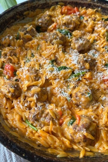 Cheesy orzo and meatballs in skillet.