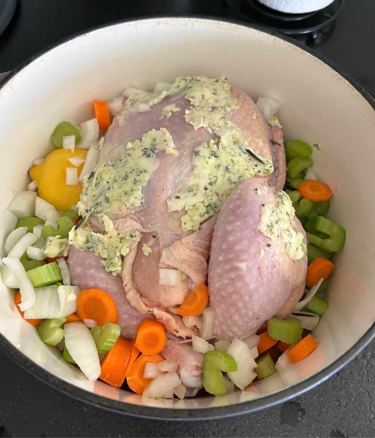 Raw whole chicken in Dutch Oven with garlic herb butter and veggies.