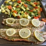 Pesto salmon with lemon slices and veggies on cookie sheet.