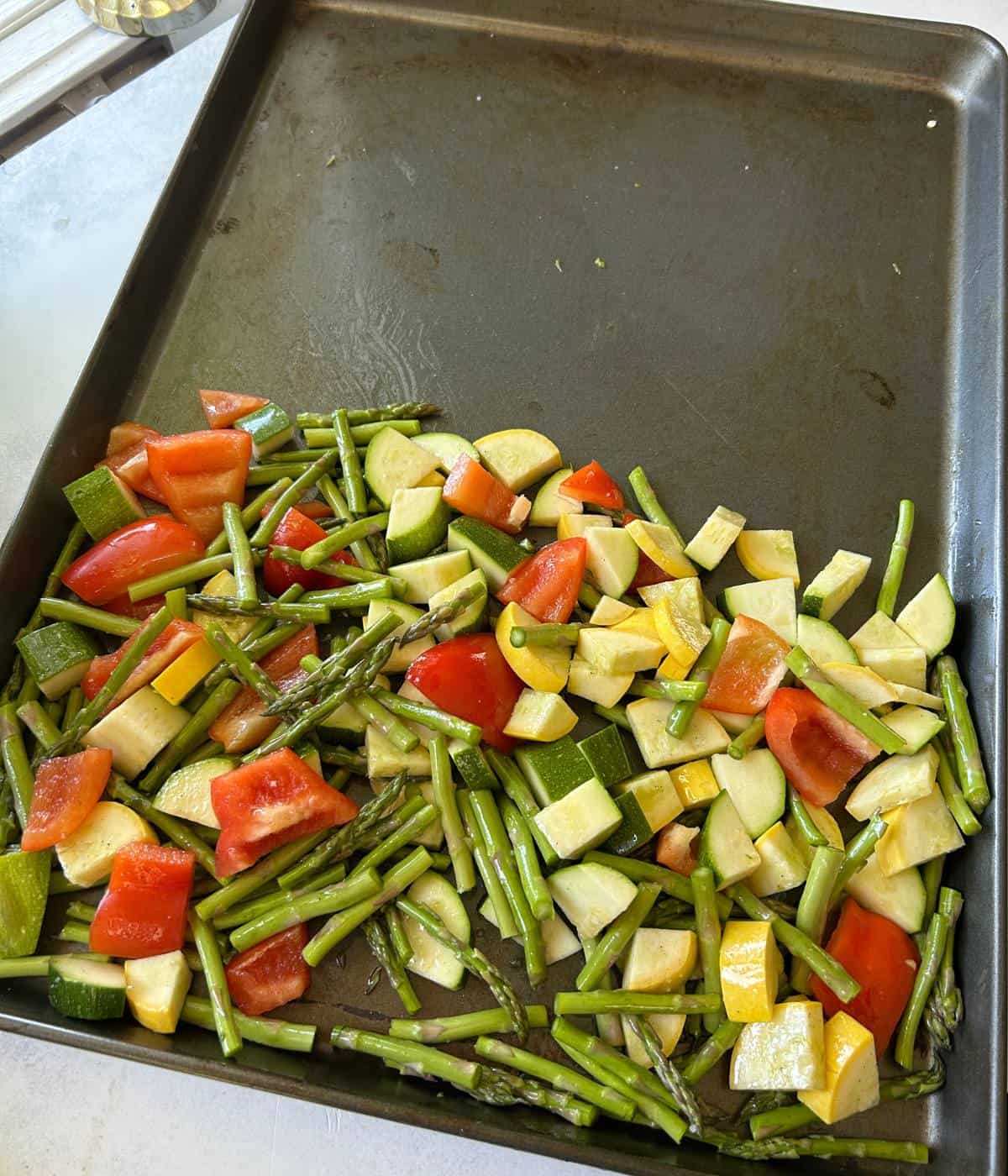 Vegetables tossed in olive oil on cookie sheet.