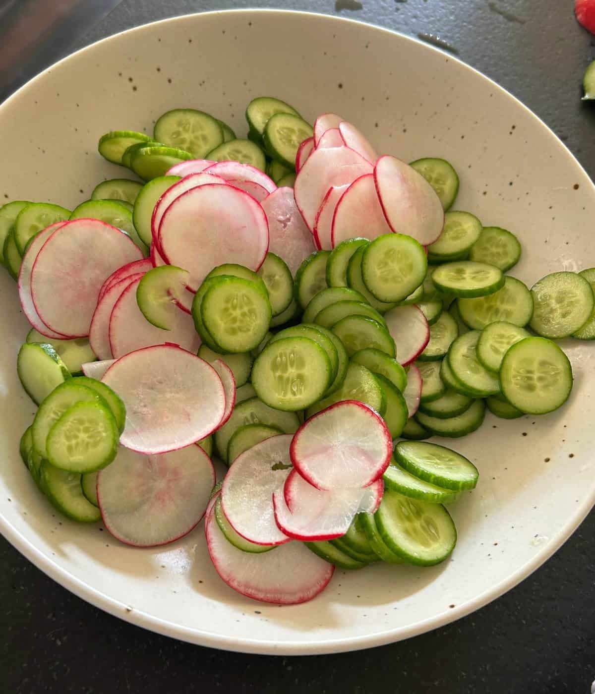 Thinly sliced radish and cucumbers in bowl.