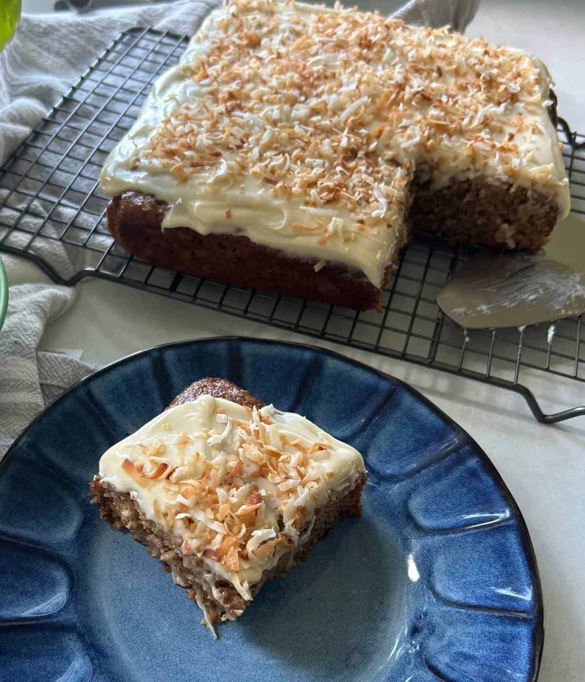 Banana cake slice topped with cream cheese frosting and toasted coconut.