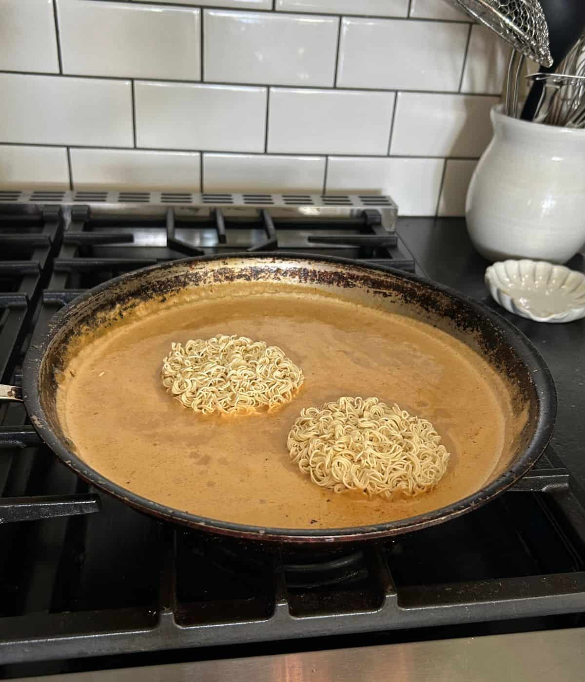 Ramen noodles cooking in bone broth in a skillet.
