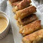 Cheeseburger egg rolls on serving plate with sauce.