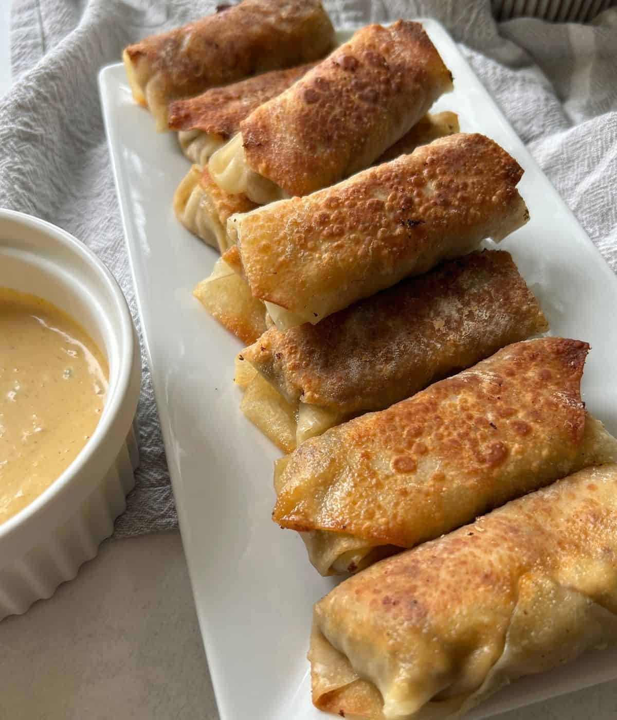 Cheeseburger egg rolls on serving plate with sauce.